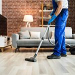 Professional cleaner vacuuming living room floor during standard cleaning vs deep cleaning service comparison